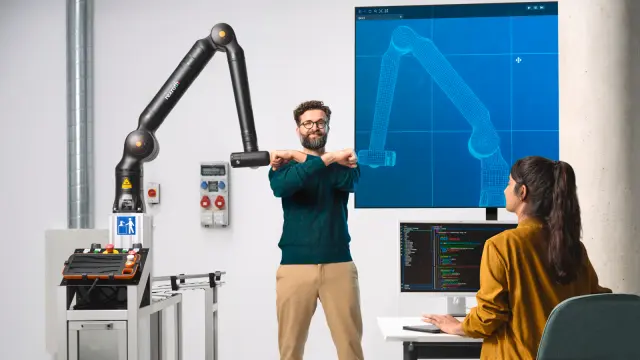 Twee medewerkers spelen aan een voetbaltafel met een Bosch Rexroth APAS assistentierobot.